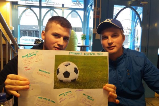 Two boys, one holding a poster with a football and ideas around it
